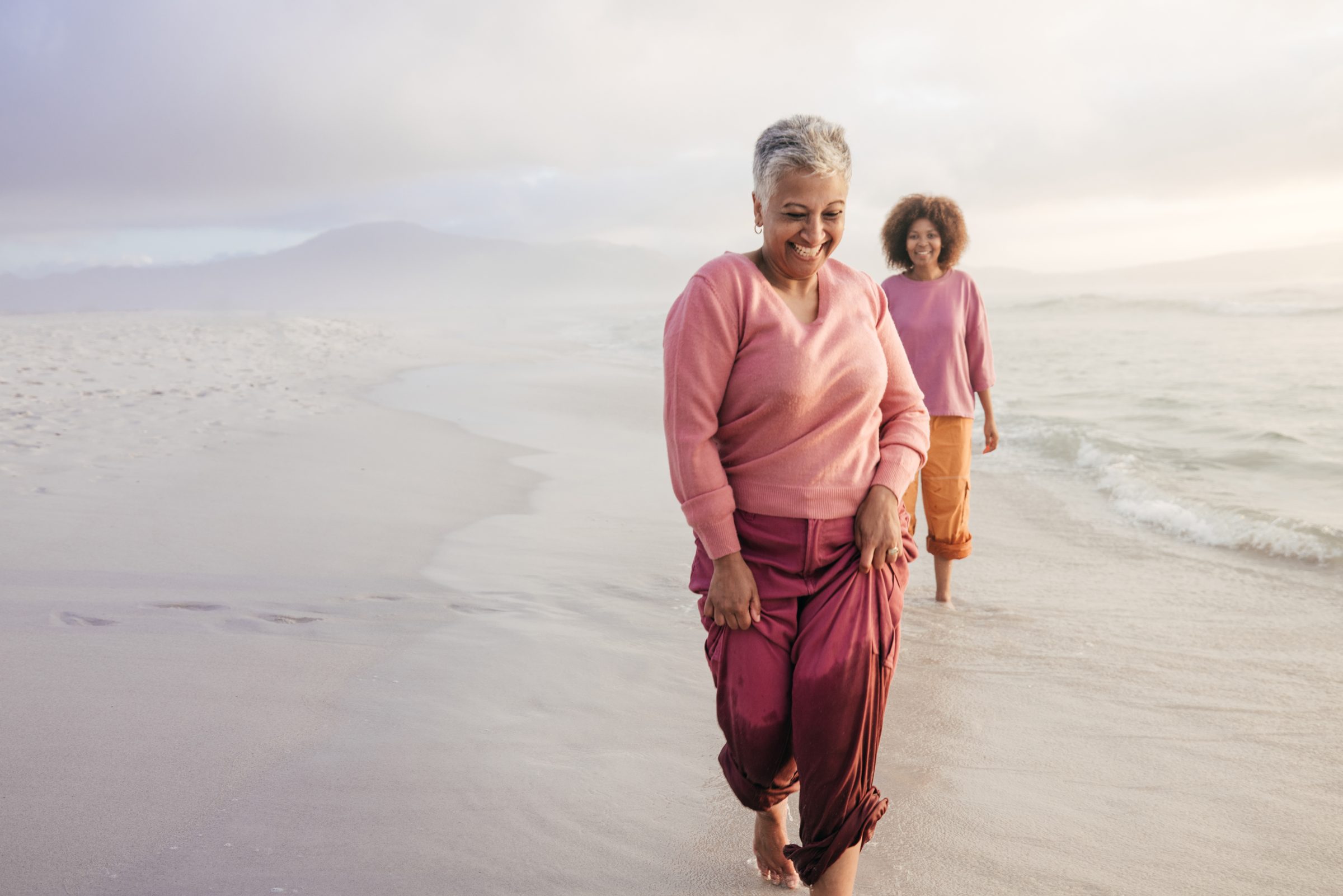 Two women walking together along a beach at dusk, smiling.