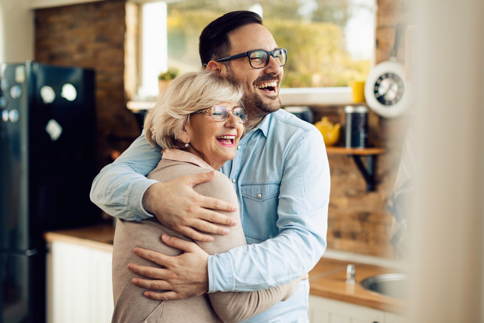 An older woman and a younger man embracing and laughing together in a kitchen.