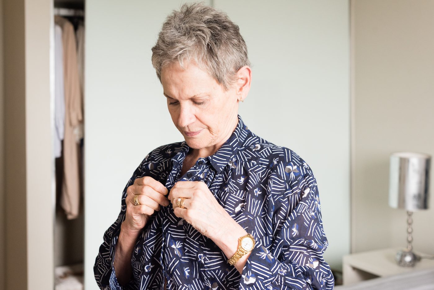 An older woman fastening the buttons on her shirt, concentrating on the small buttons.